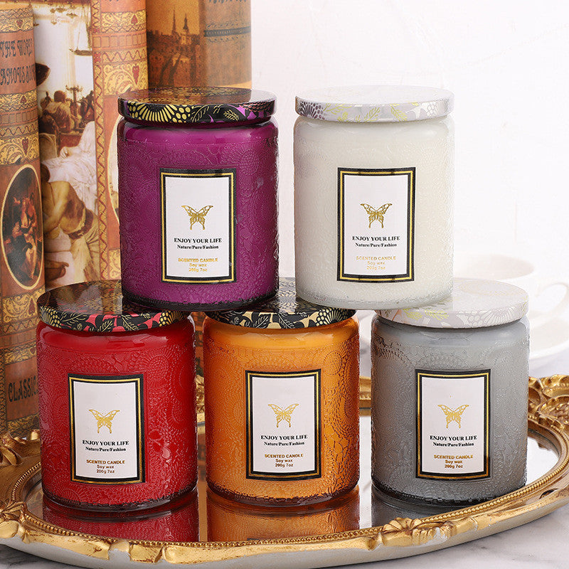 Five scented candles of different colors on a decorative tray with books in the background.