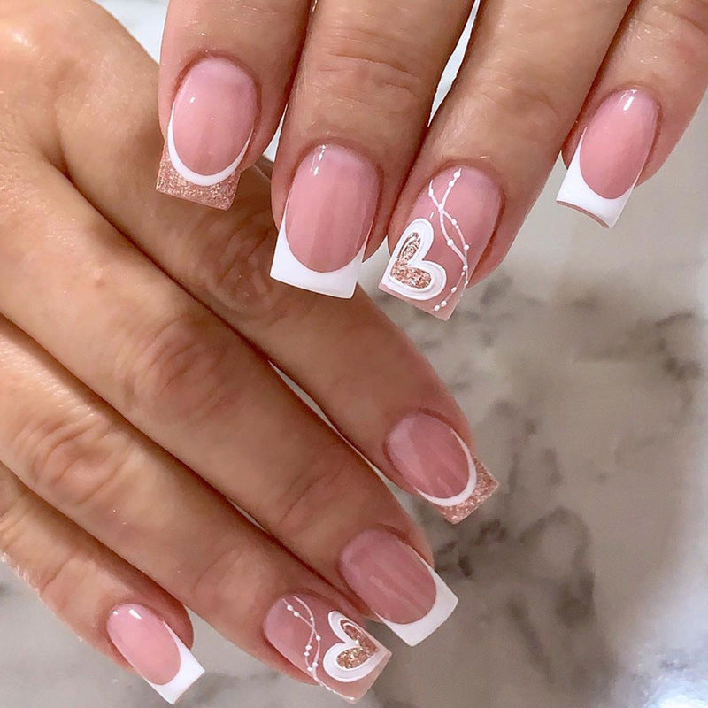 A set of false nails with a pink and white design, featuring heart patterns and glitter accents.