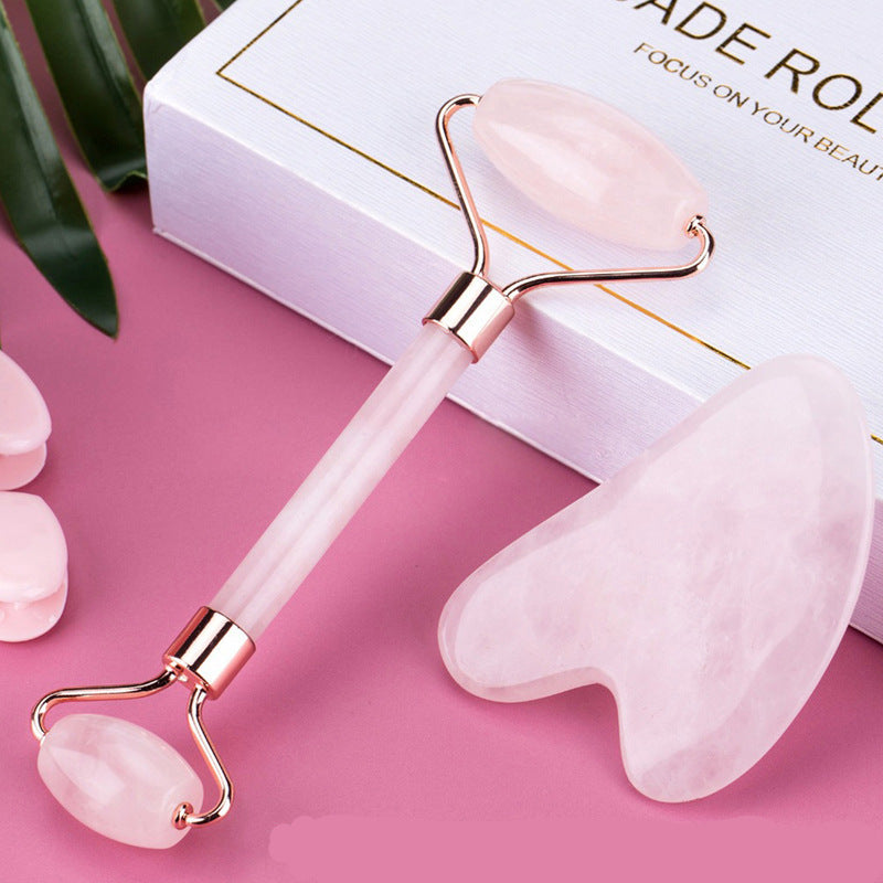 Pink facial roller and gua sha tool on a pink background with a white box.