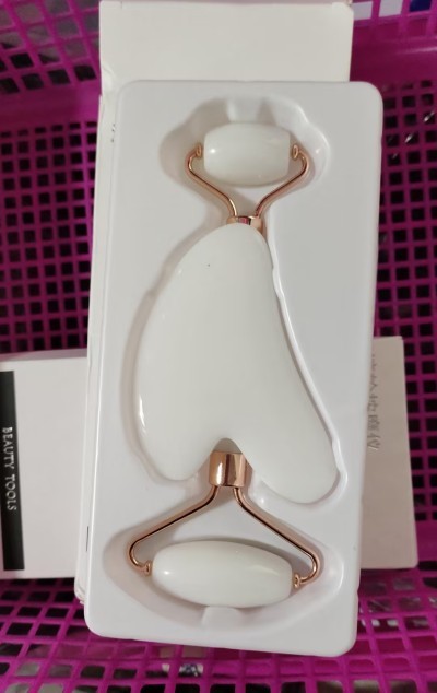 White facial roller with gold accents on a white card with a pink background