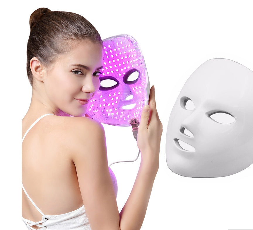 Woman holding a purple LED face mask next to a white one on a white background